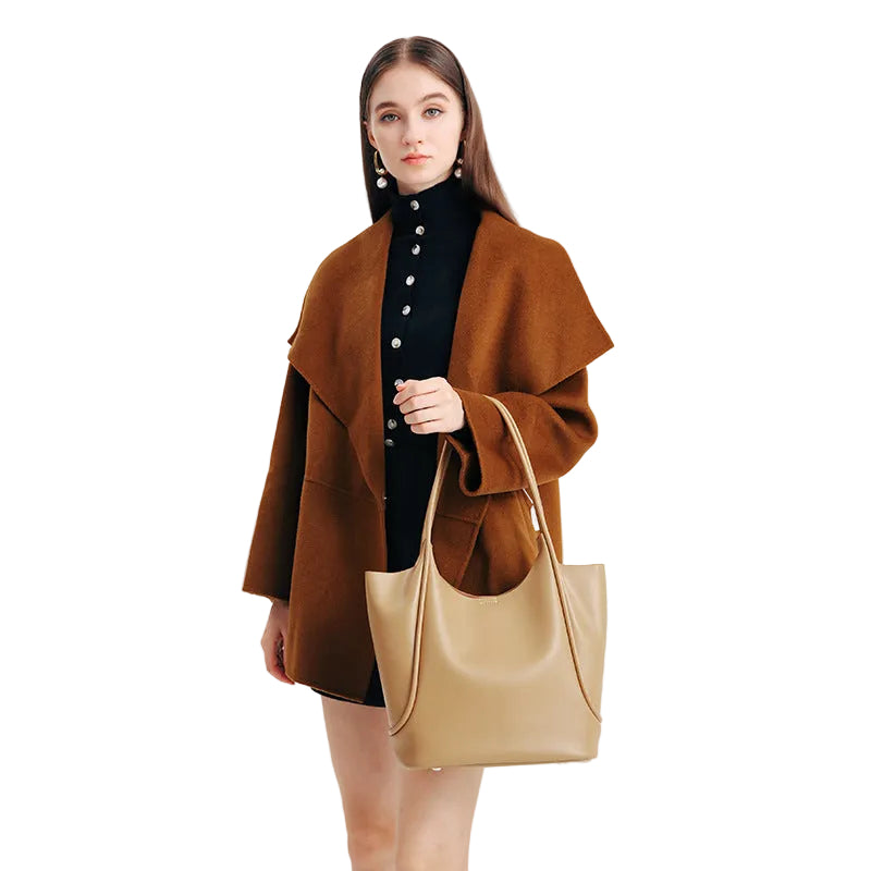 Woman holding a beige handbag wearing a brown coat on a white background