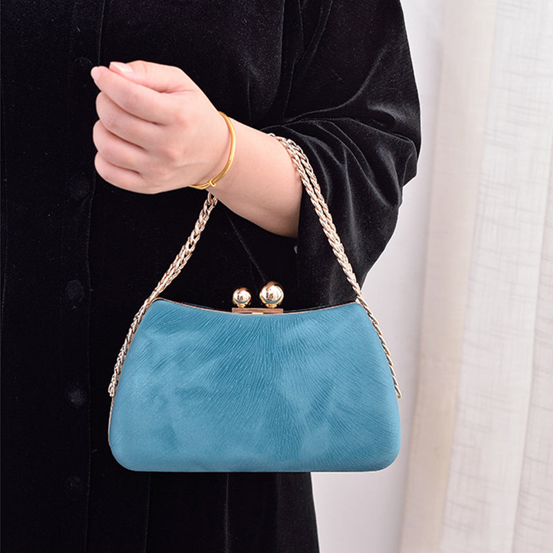 Blue handbag with gold chain strap held by a person wearing a black outfit.