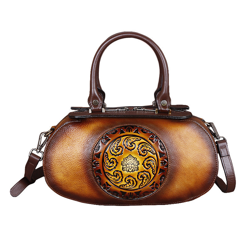 Brown leather handbag with decorative emblem on a white background