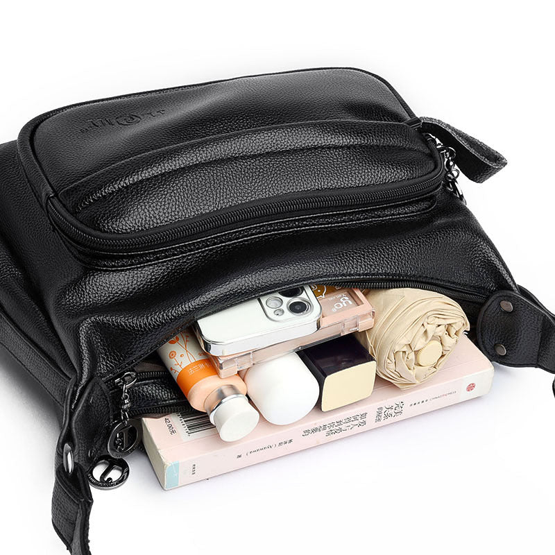 Black leather crossbody bag with items inside on a white background