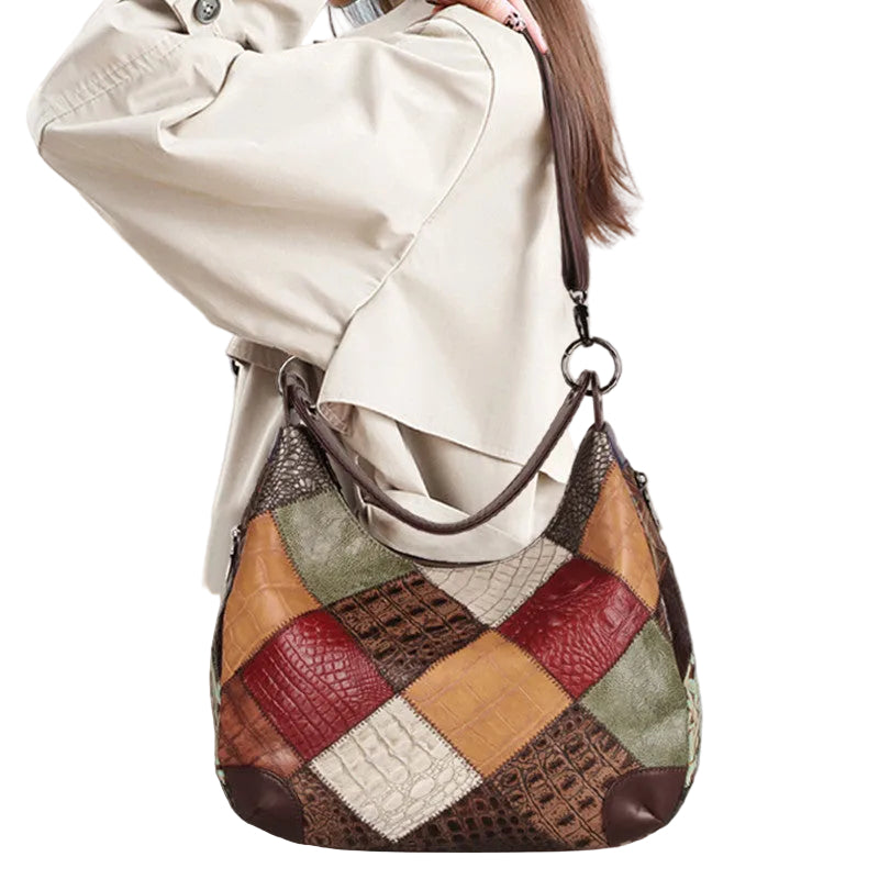Patchwork handbag held by a person wearing a beige coat against a light gray background