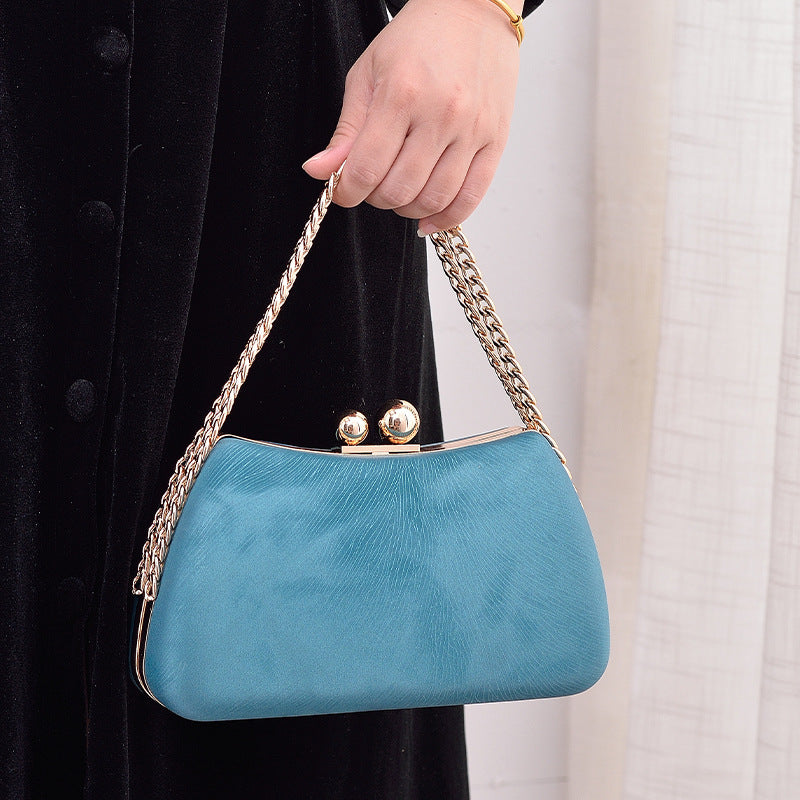 Blue handbag with gold chain handle held by a person against a neutral background