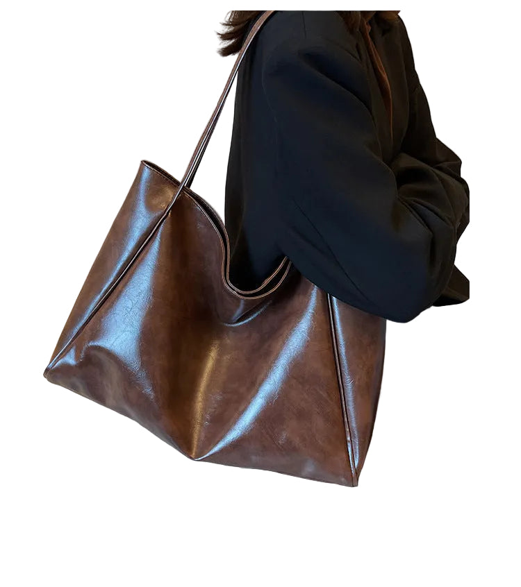 Brown leather handbag held by a person wearing a black coat against a white background.