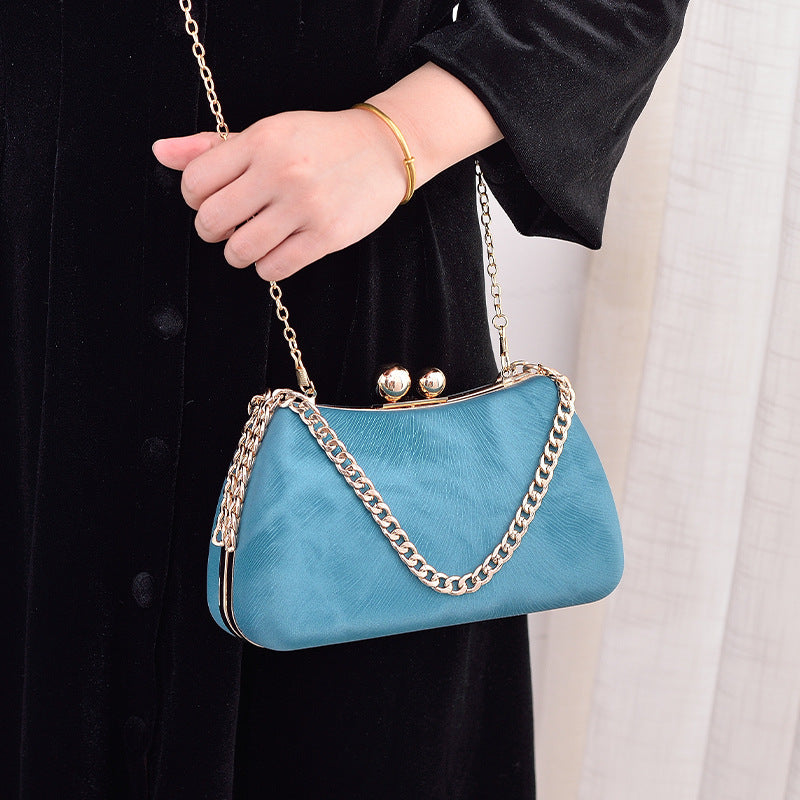 Blue handbag with gold chain strap held by a person wearing a black coat.