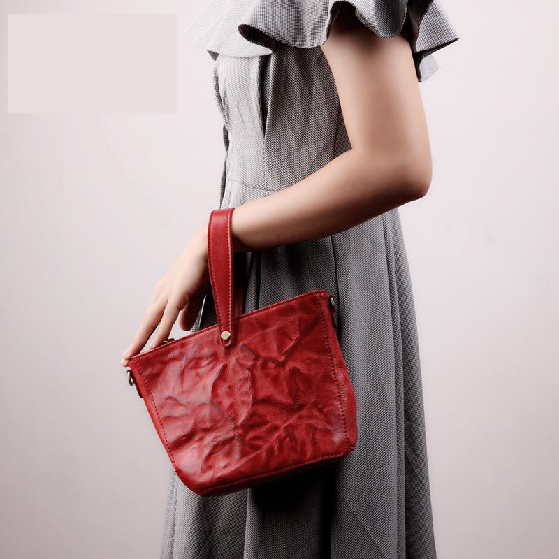 Red textured handbag held by a person wearing a gray dress against a light background