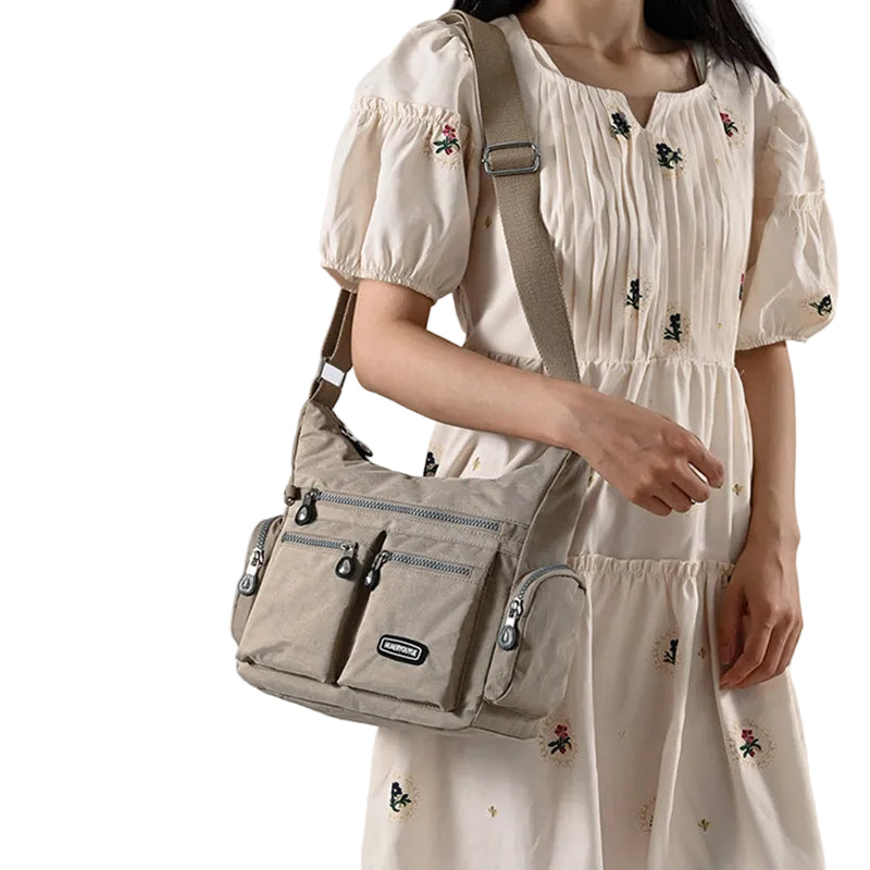 Person wearing a beige dress with floral embroidery holding a beige shoulder bag against a white background