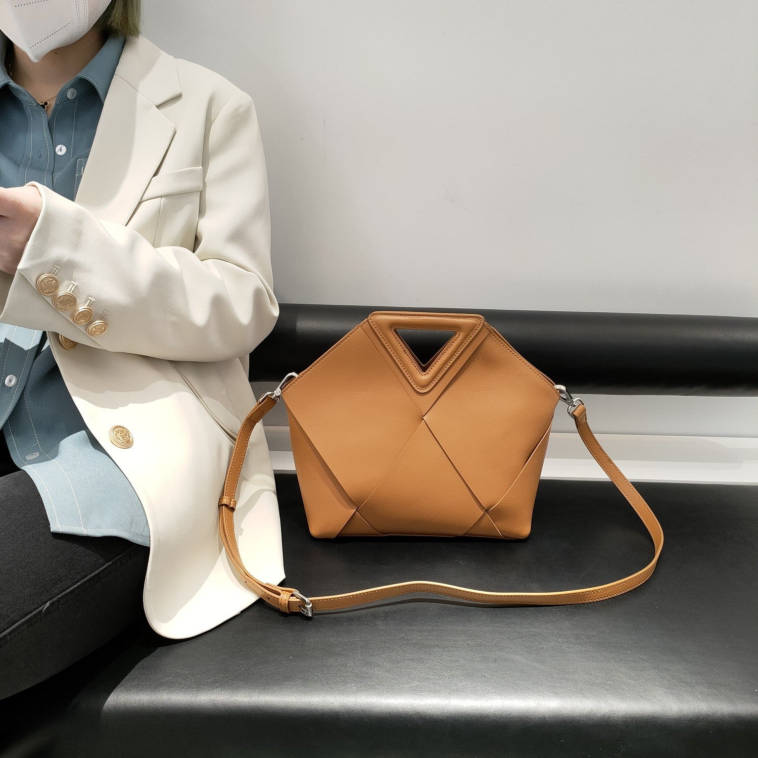 Person wearing a beige blazer with a quilted brown handbag on a black surface.