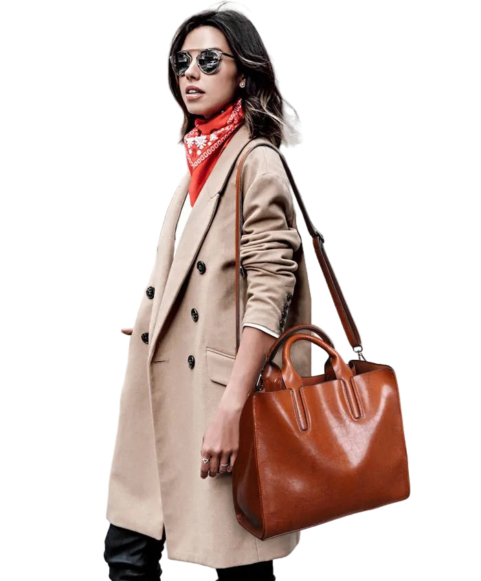Woman in a beige coat holding a brown leather bag on a white background