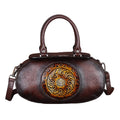 Brown leather handbag with decorative emblem on a white background