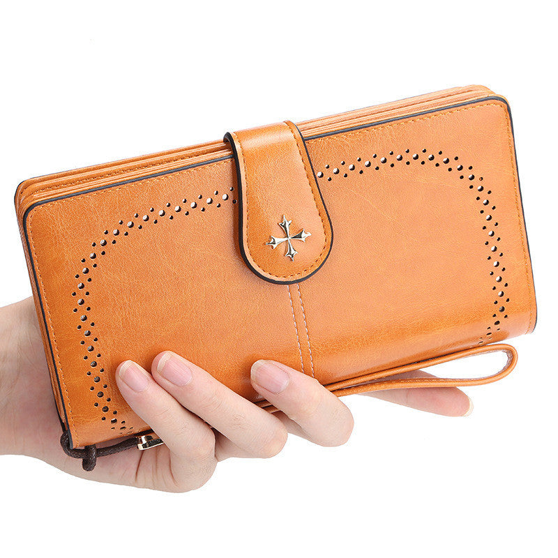 Hand holding a brown leather wallet with decorative cutouts on a white background