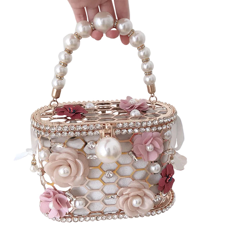 Decorative handbag with floral and pearl details held by a hand against a white background