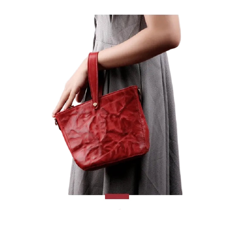 Red handbag held by a person wearing a gray dress on a white background