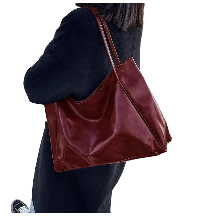 Person holding a brown leather tote bag on a white background